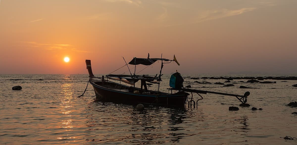 A longtail boat silhouetted at sunset off Klong Khong Beach, Koh Lanta